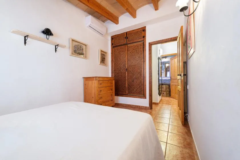 Un dormitorio con una cama, una cómoda de madera y una puerta abierta.