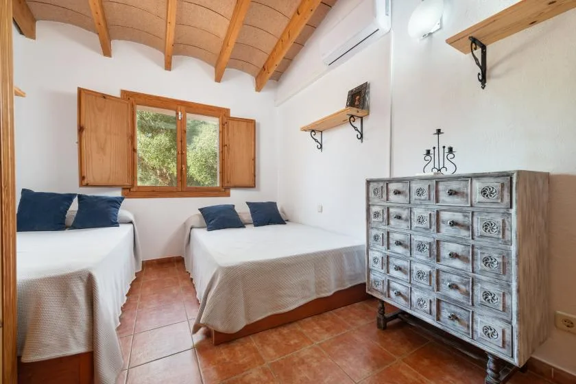 Un dormitorio luminoso con dos camas, techo de madera y una ventana.