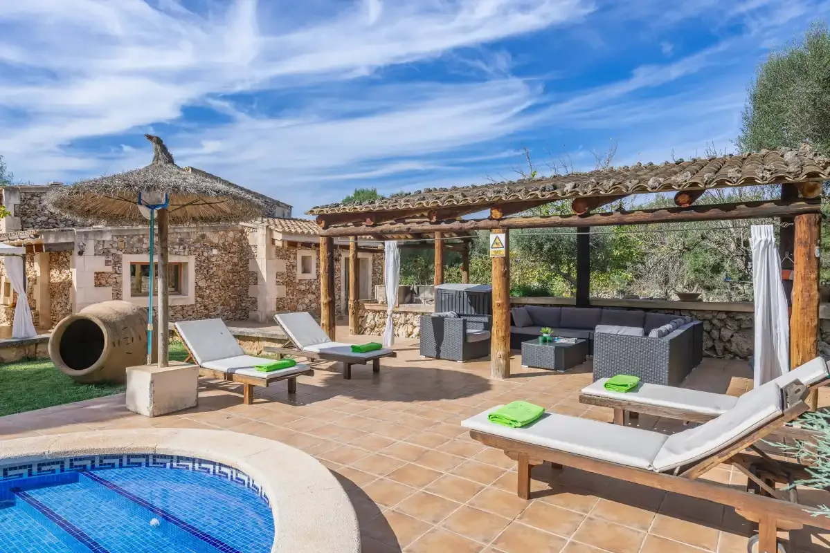 Un patio embaldosado con piscina, tumbonas y una zona de comedor a la sombra.