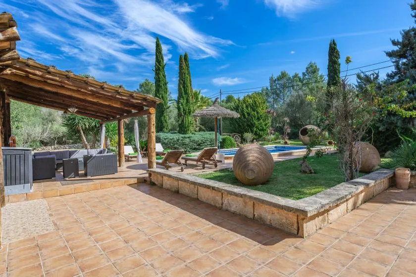 Un patio ajardinado con asientos, una pérgola y una piscina.