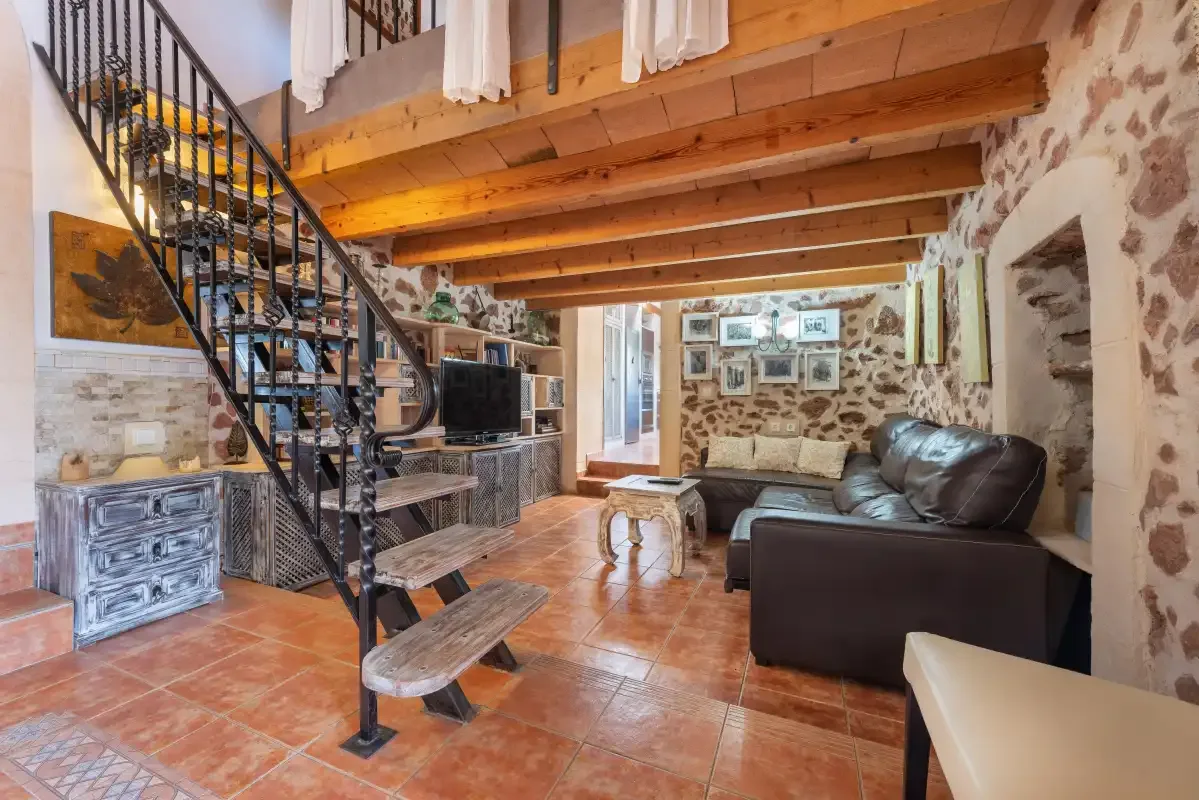 Sala de estar con asientos, un televisor y una escalera bajo vigas de madera vistas.