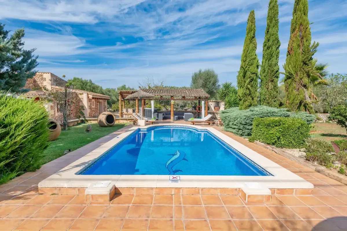 Una piscina exterior está junto a una zona de estar cubierta y un jardín cuidado.