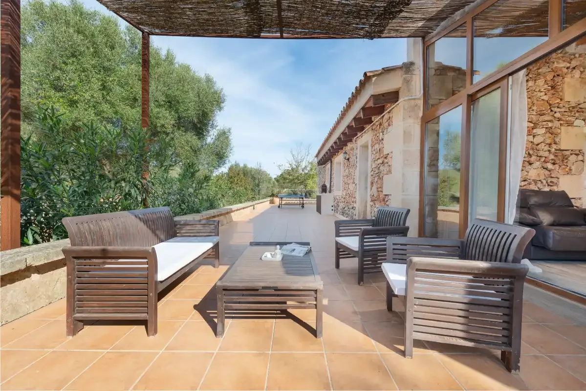 Un patio de baldosas con asientos exteriores junto a un edificio de piedra y puertas de cristal.