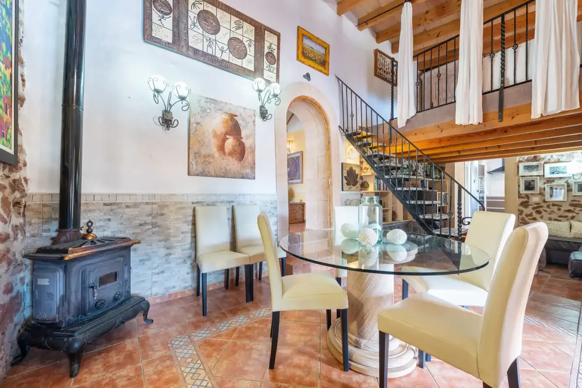 Un comedor con una mesa de vidrio y una escalera que sube a un balcón de madera.