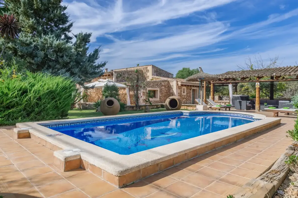 Una piscina al aire libre está junto a un edificio de piedra y un patio pavimentado.