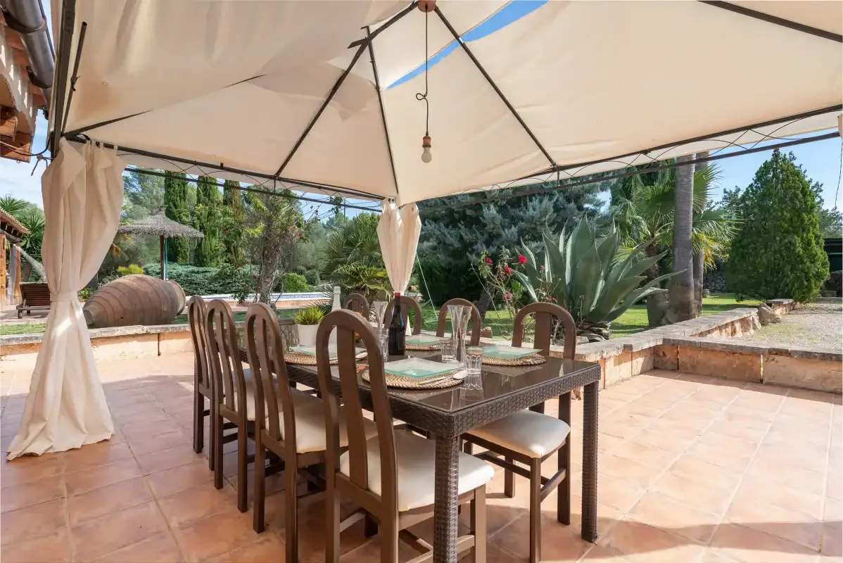 Una zona de comedor exterior cubierta, con mesa y sillas, da a un jardín ajardinado.
