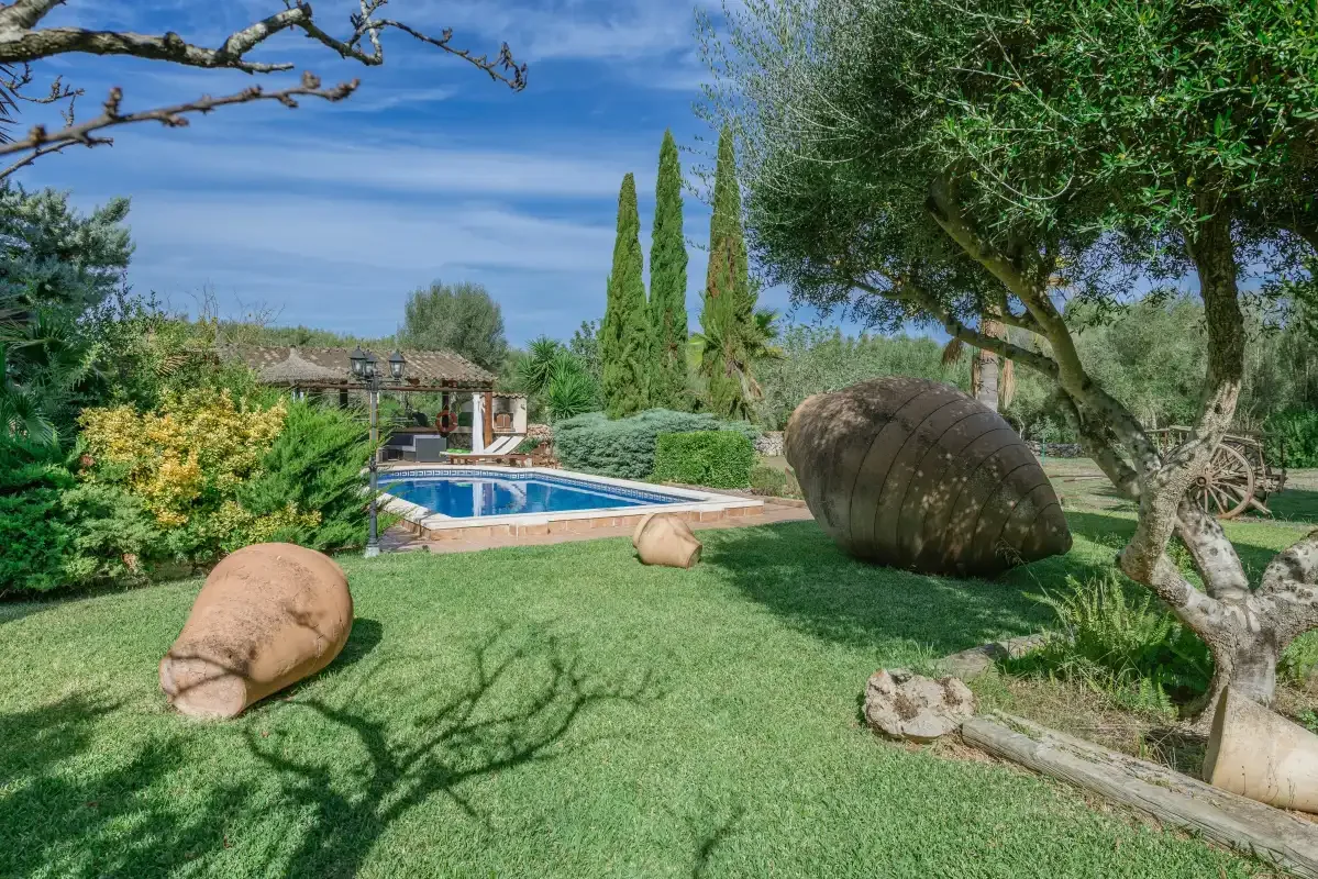 Un jardín paisajístico rodea una piscina, con árboles y formas escultóricas de piedra.