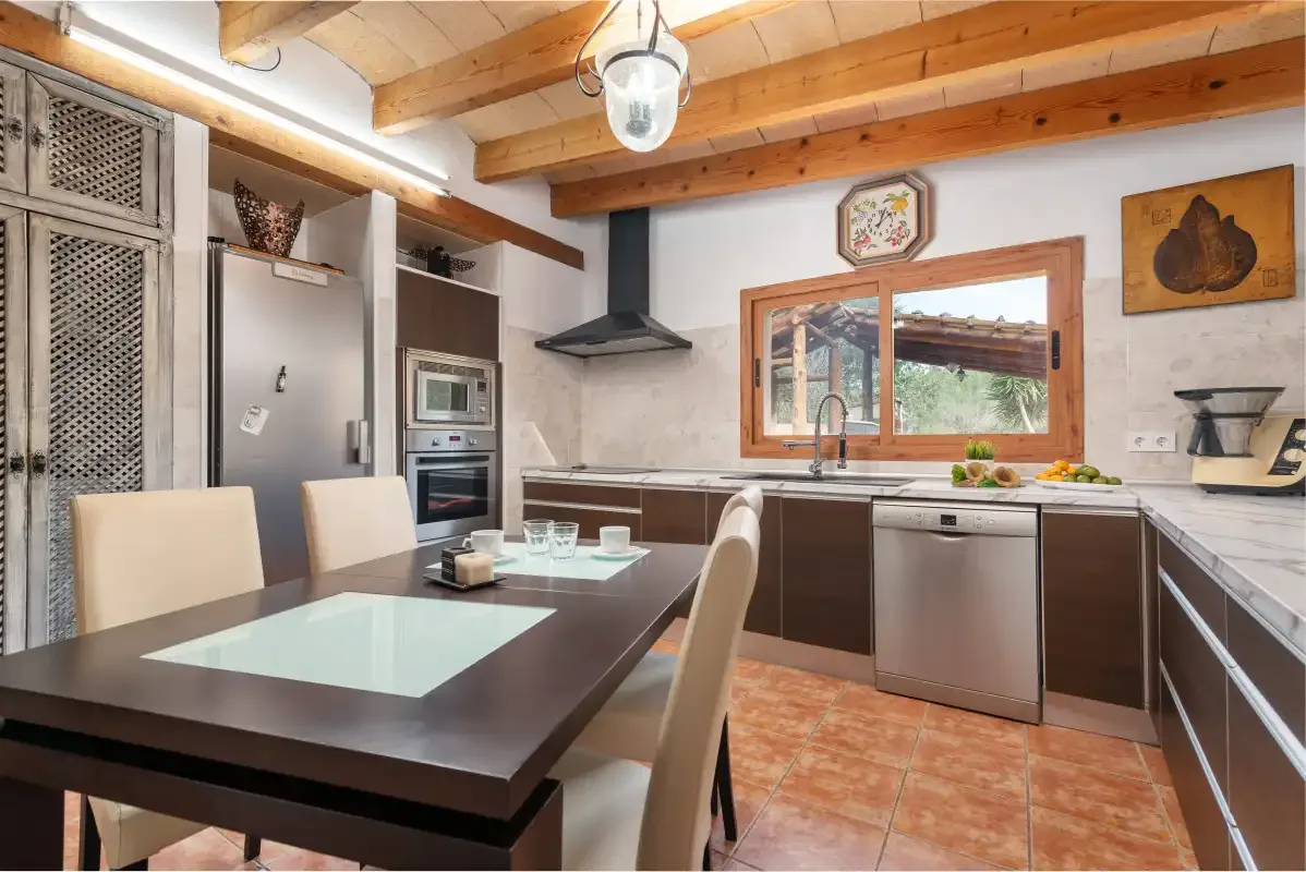 Una cocina luminosa con mesa de comedor, electrodomésticos empotrados y vigas de madera.