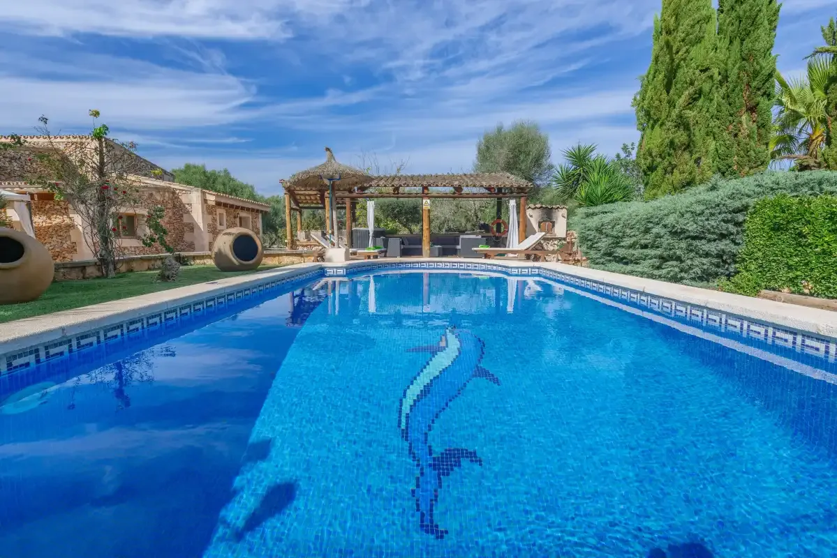 Una piscina al aire libre con un mosaico de delfín y una pérgola al fondo.
