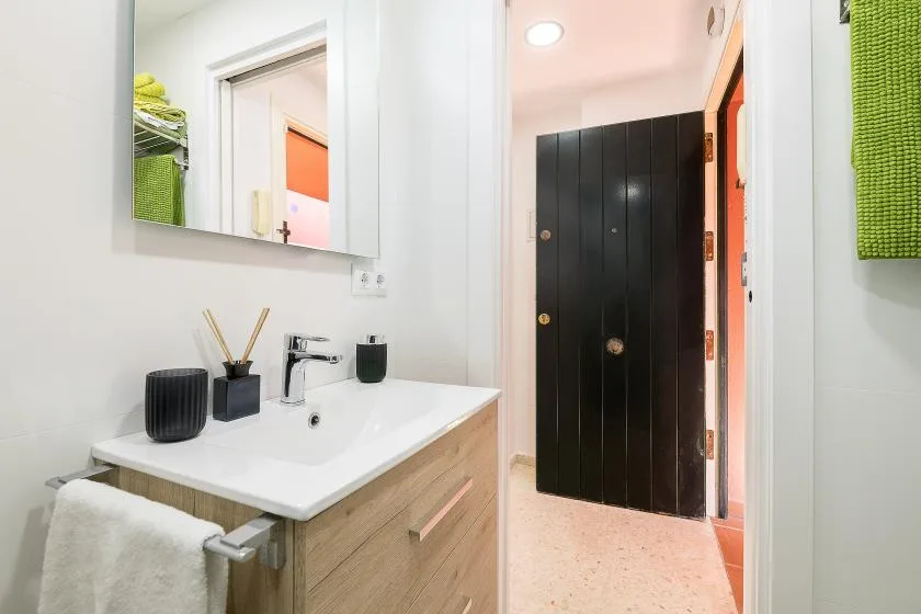 A bathroom vanity with a sink and mirror faces an open doorway.