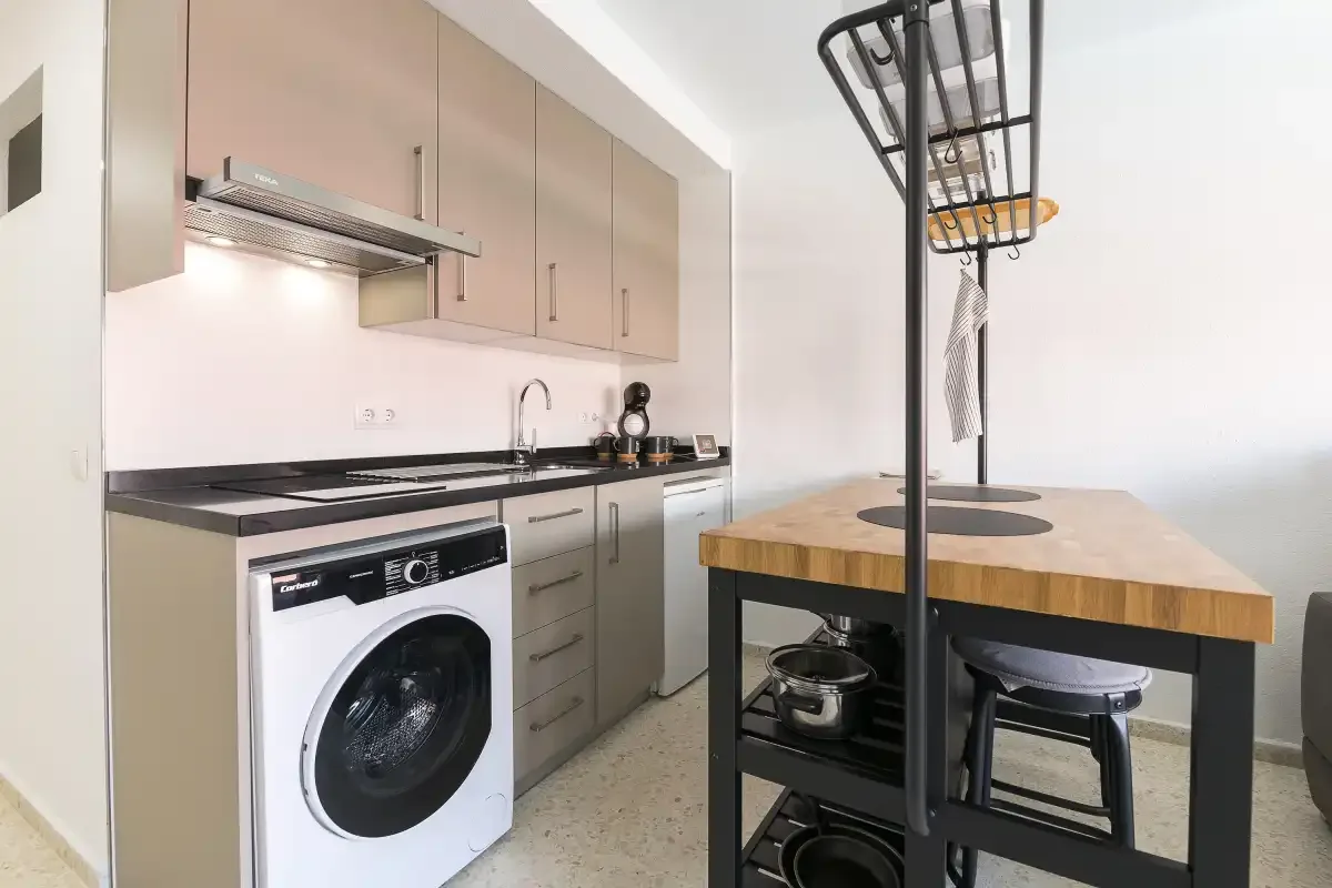 A modern kitchen with a washing machine beneath the counter and a wooden island.