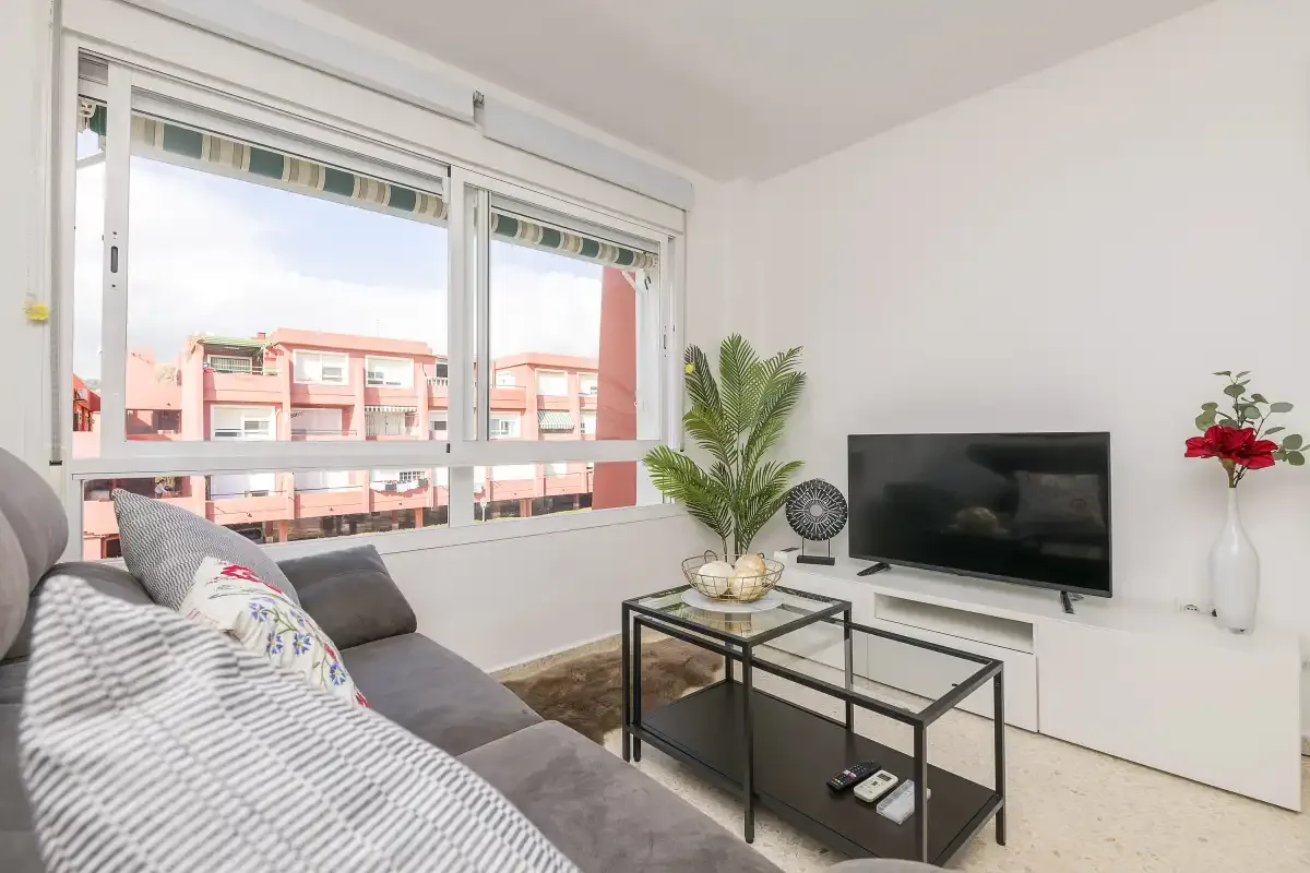 A bright living room with seating, a television, and large windows.