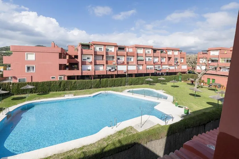 A swimming pool sits in a landscaped courtyard surrounded by pink apartment buildings.