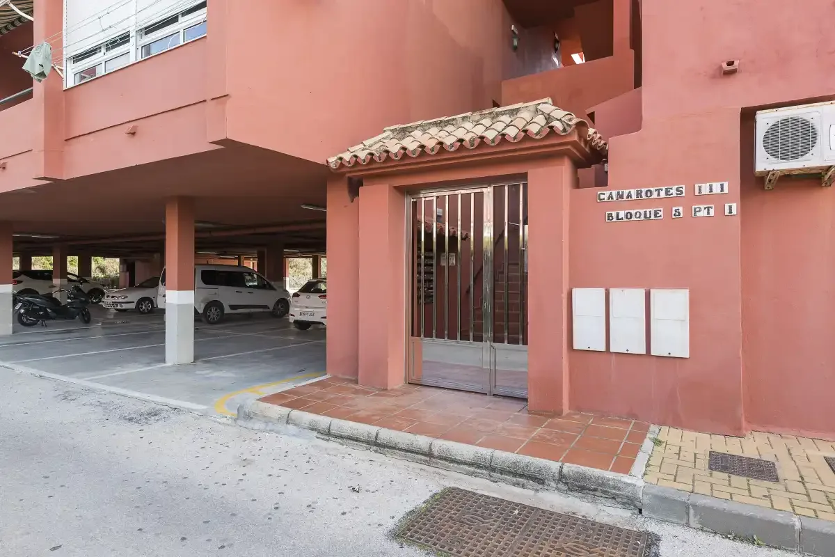 A pink apartment building entrance with a barred glass door and covered parking.