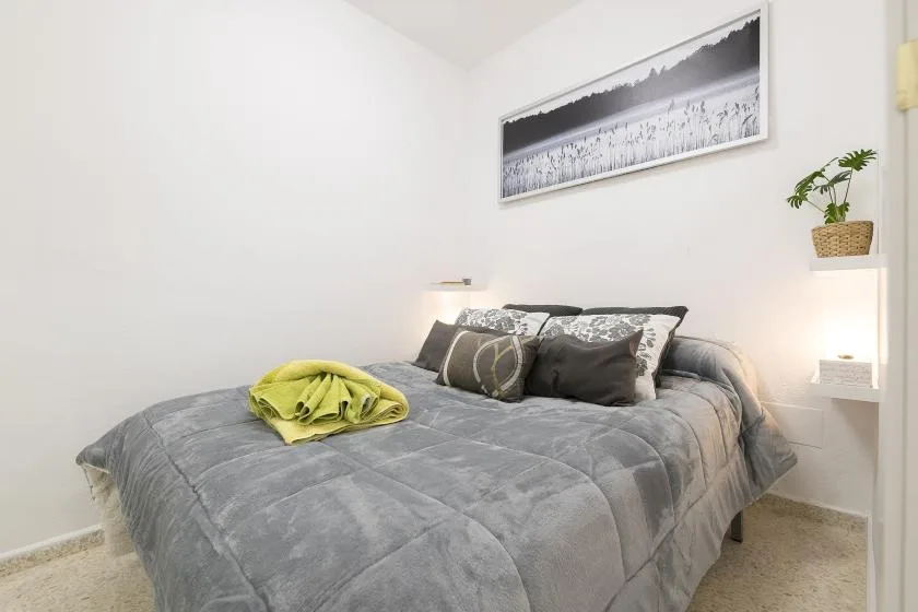 A bedroom with a gray bedspread, pillows, and a framed wall photograph.