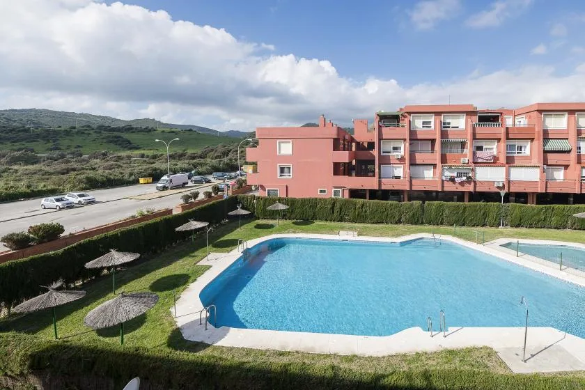 Piscina al aire libre junto a un edificio de varias plantas, con colinas verdes al fondo.