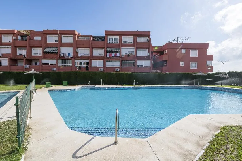 An outdoor swimming pool sits in front of a row of red-brick apartment buildings.