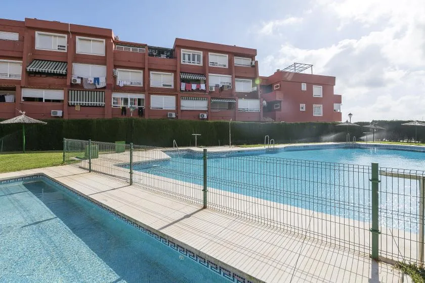 An outdoor swimming pool sits beside a paved deck and residential buildings.