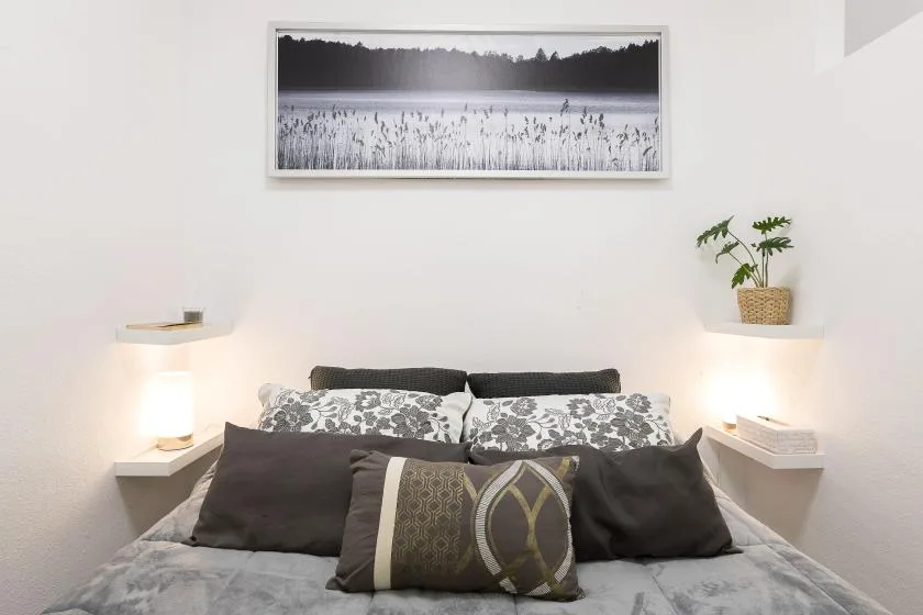 A bedroom with a bed, patterned pillows, and a framed landscape photograph.