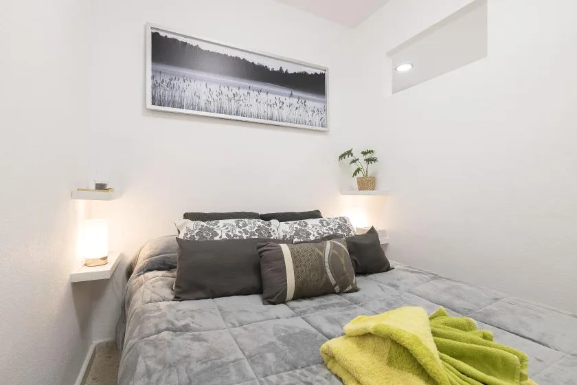 A bedroom with a neatly made bed and a framed landscape photograph above it.