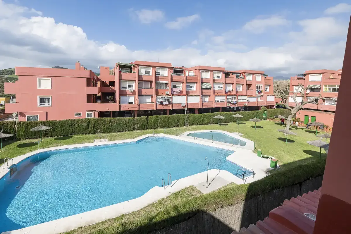 An outdoor swimming pool sits beside a grassy courtyard and apartment buildings.