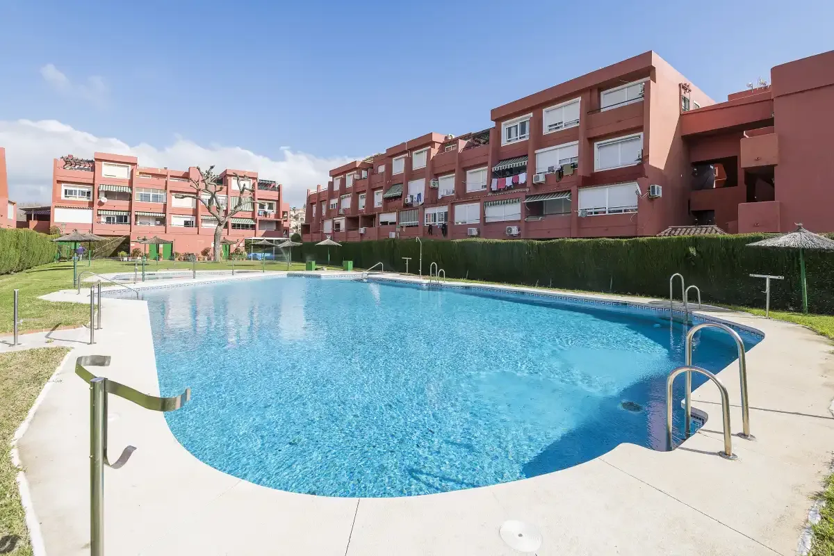 An outdoor swimming pool sits beside a row of apartment buildings.