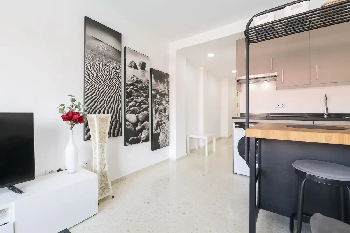 A bright living area opens onto a compact kitchen with a counter and seating.