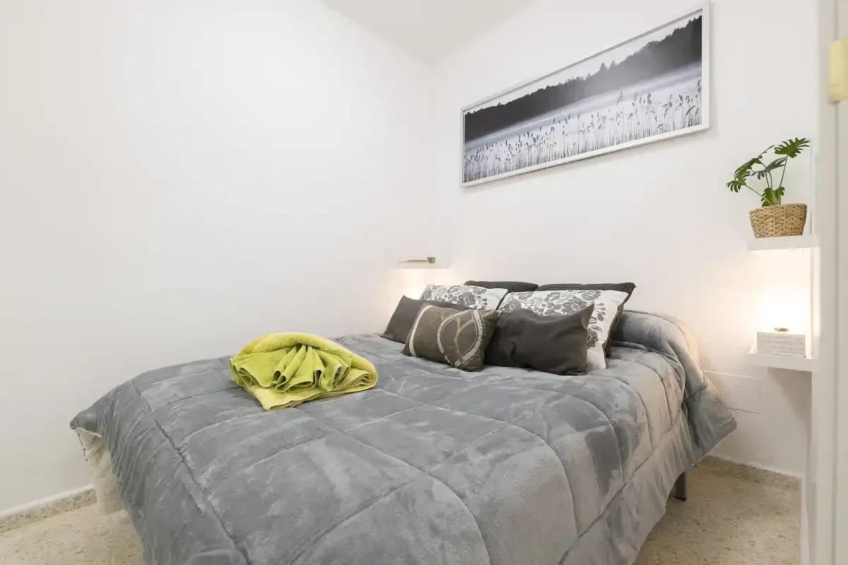 A bedroom with a gray bedspread and framed wall art.