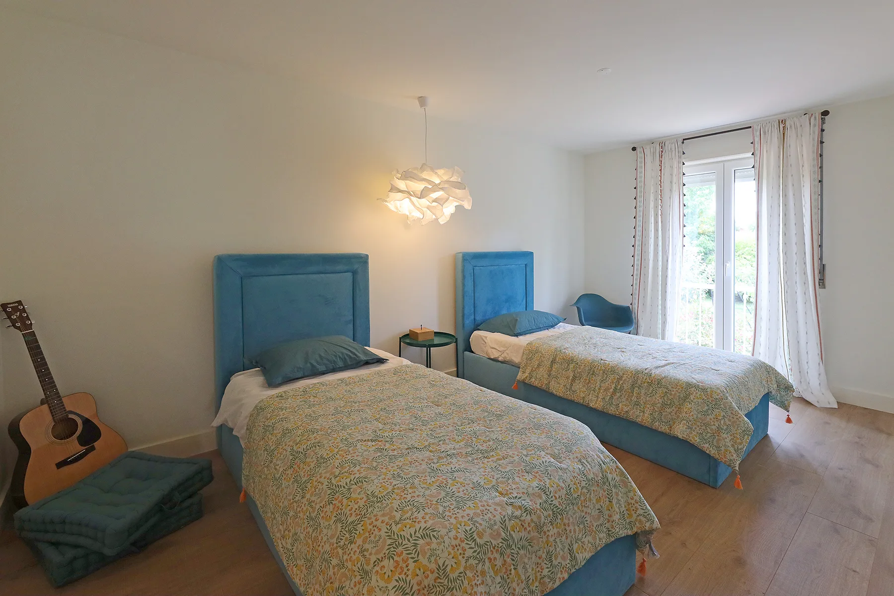 A bedroom with two beds, patterned bedding, and a window with curtains.