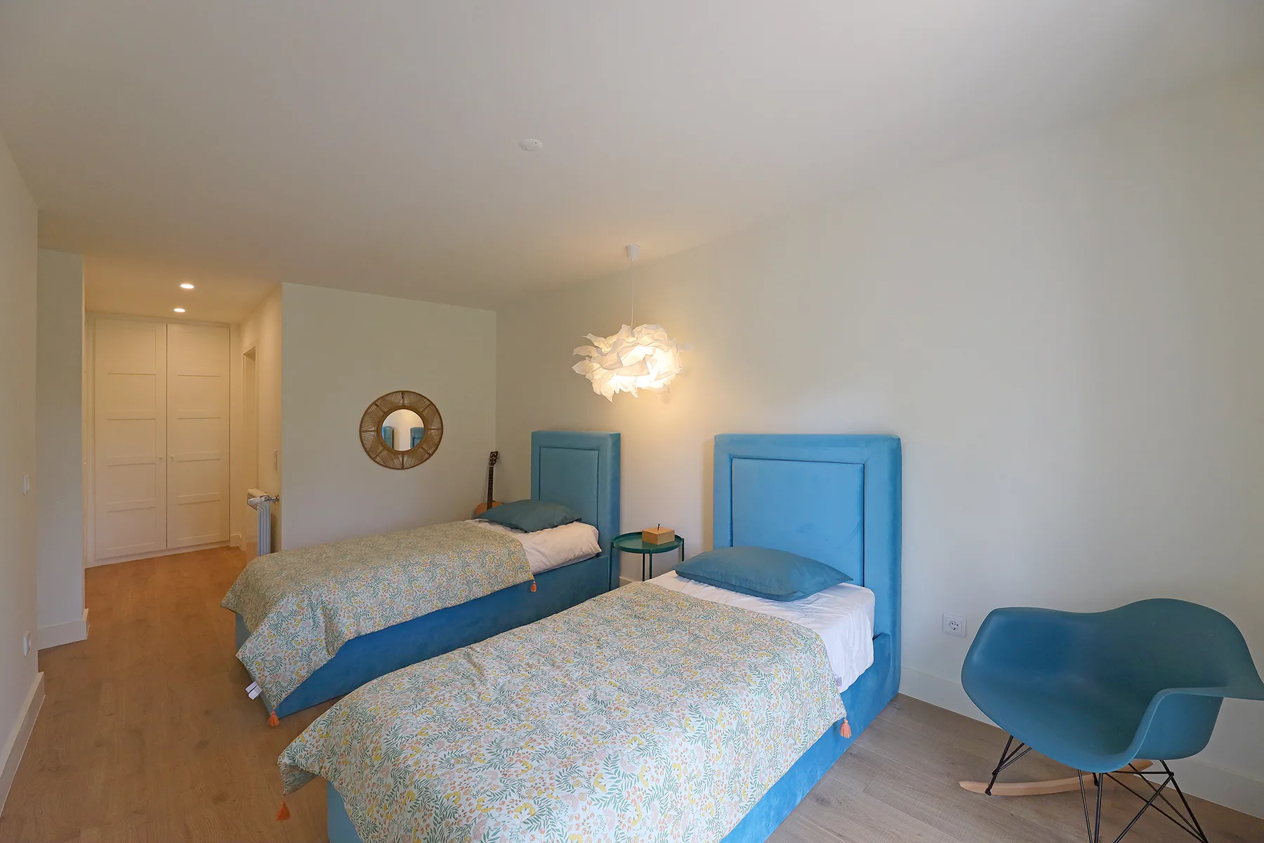 A bedroom with two beds, blue headboards, and a blue chair.