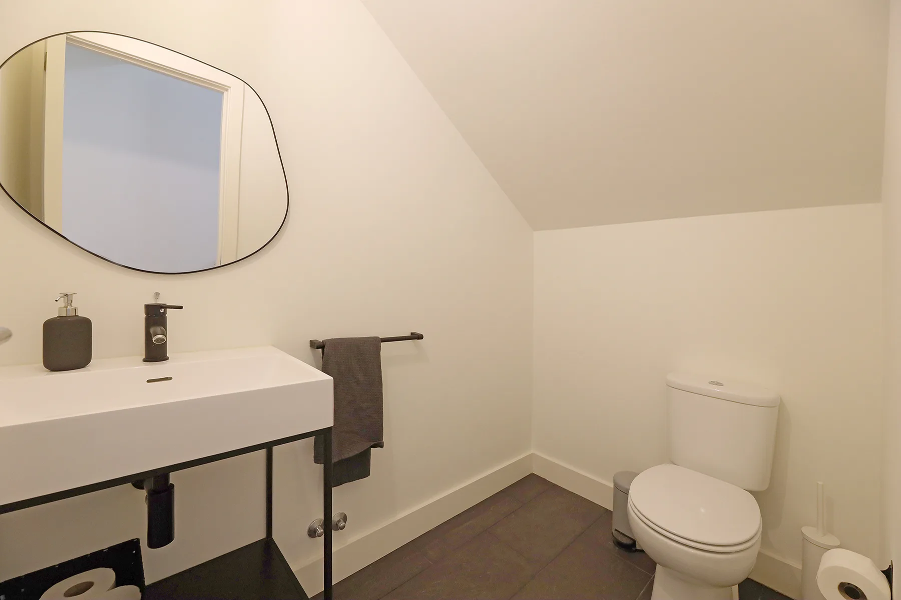 A bathroom with a sink, oval mirror, and toilet.