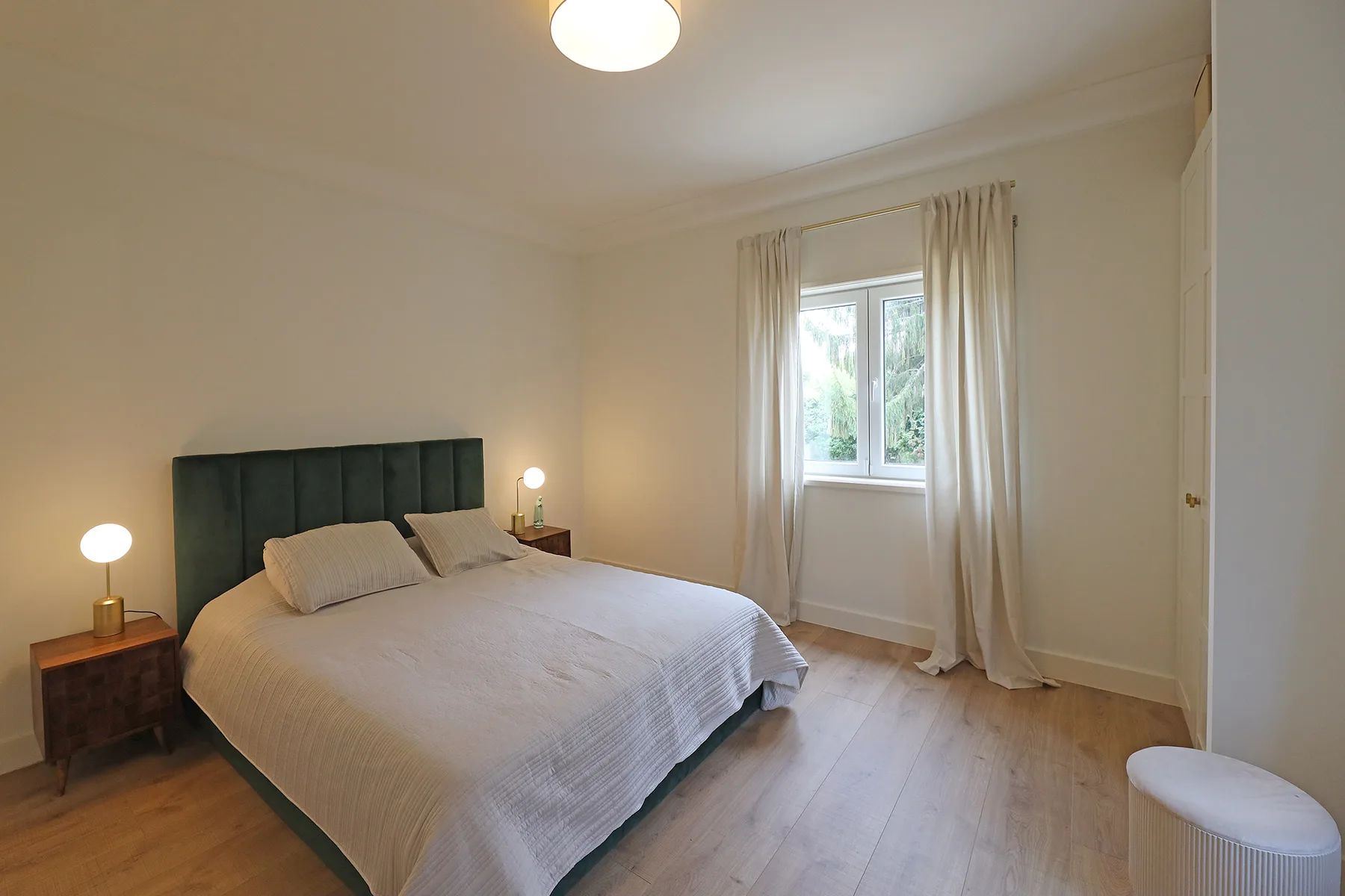 A bedroom with a bed beside a window dressed with curtains.