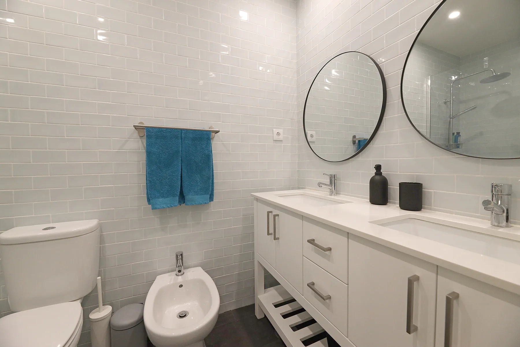 A tiled bathroom with a toilet, bidet, and long vanity.