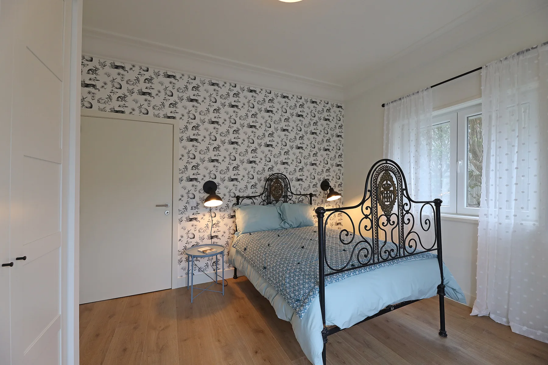A bedroom with a wrought-iron bed and patterned wallpaper.