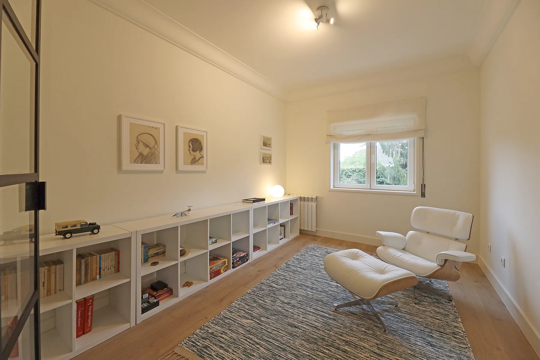 A bright living room with low shelving and a seating area beside the window.