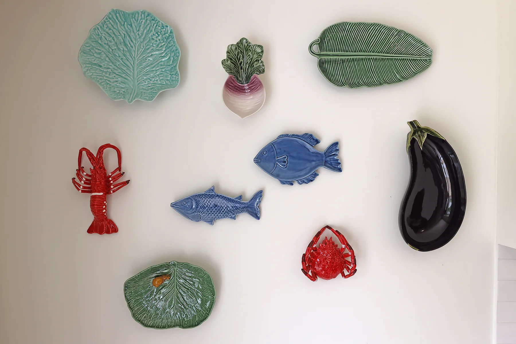 Decorative ceramic sea-life and vegetable pieces hang on a light-colored wall.