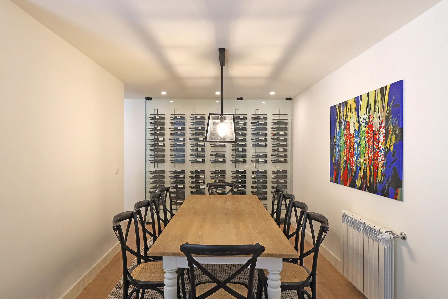 A long dining table with chairs sits beneath a pendant light in a bright room.