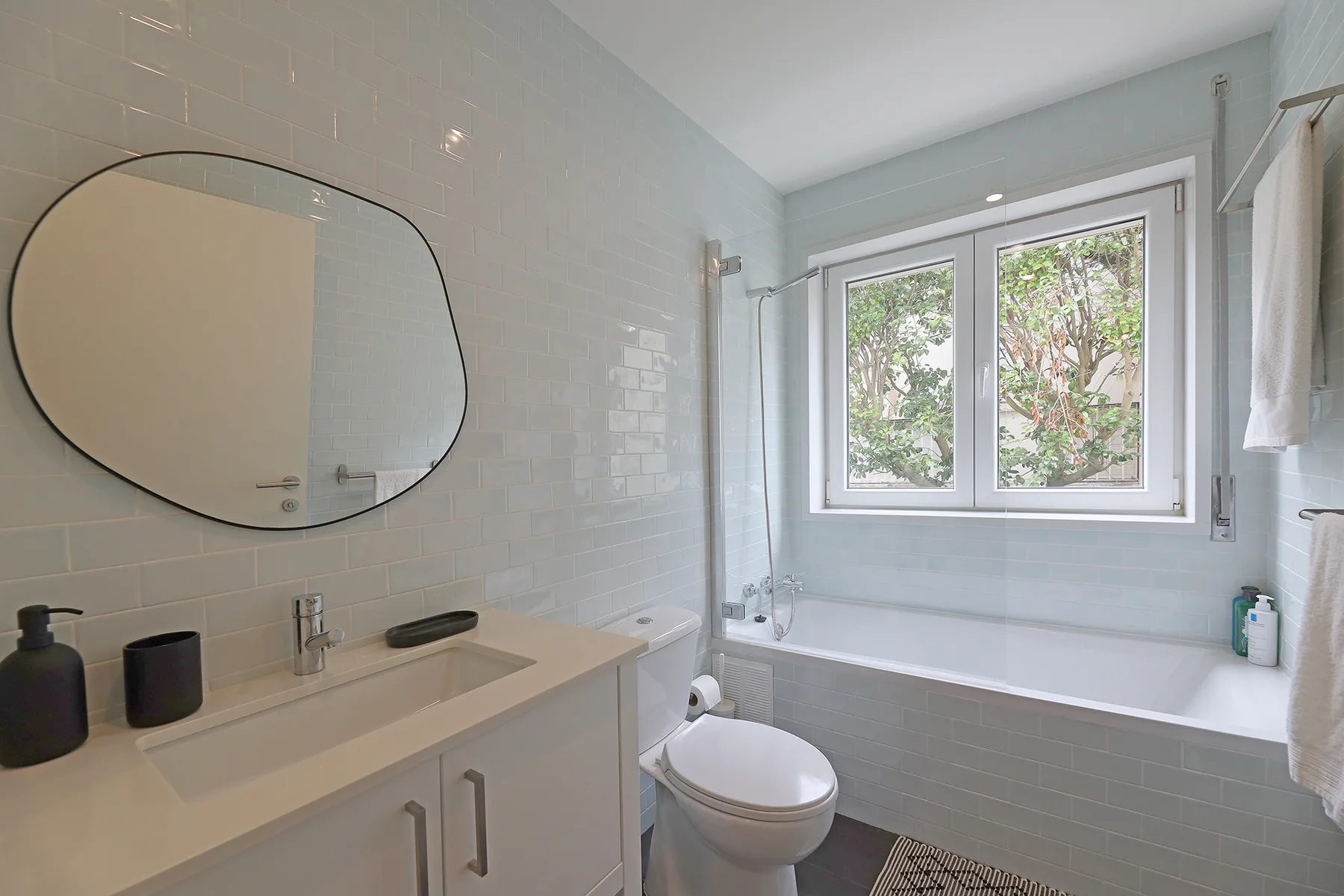 A bright bathroom with a sink, toilet, and bathtub beneath a window.