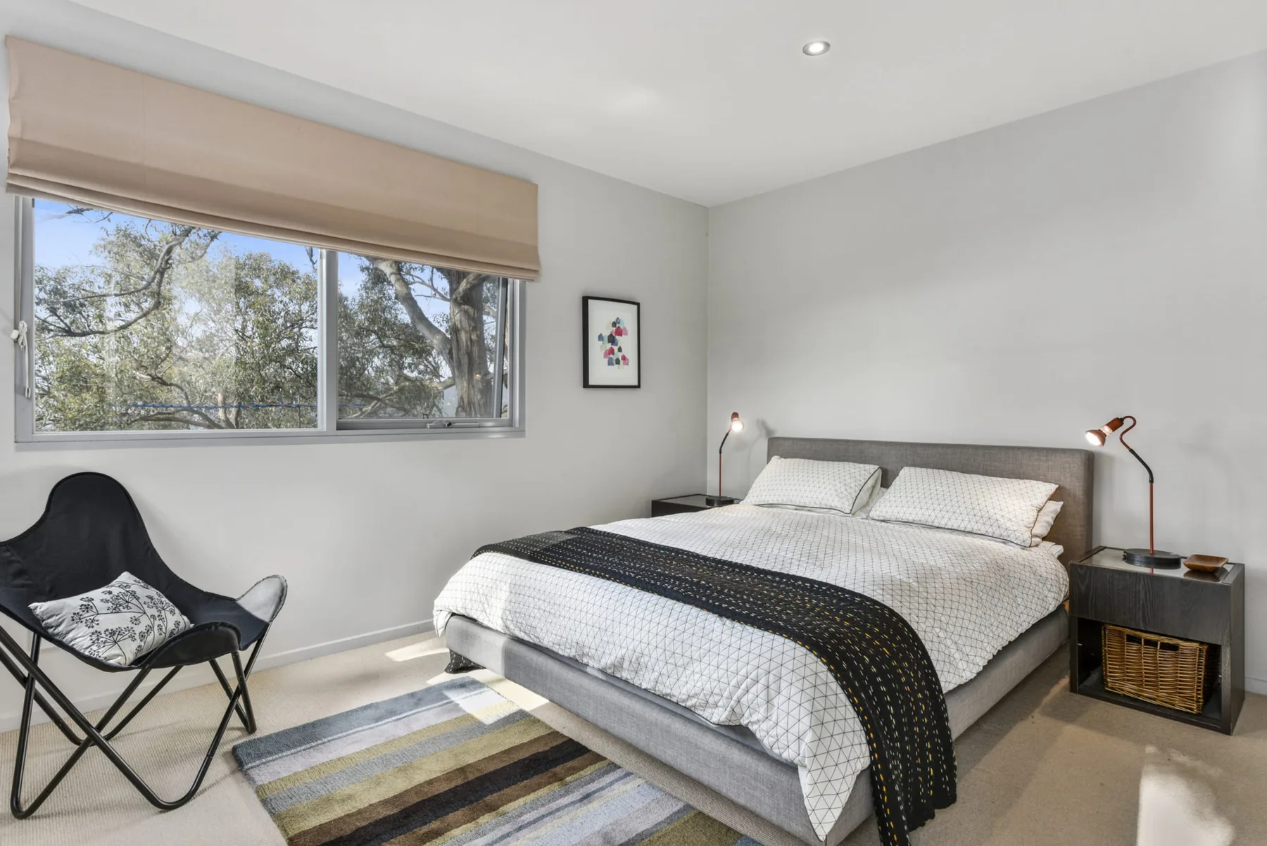 A bright bedroom with a double bed and a large window overlooking trees.