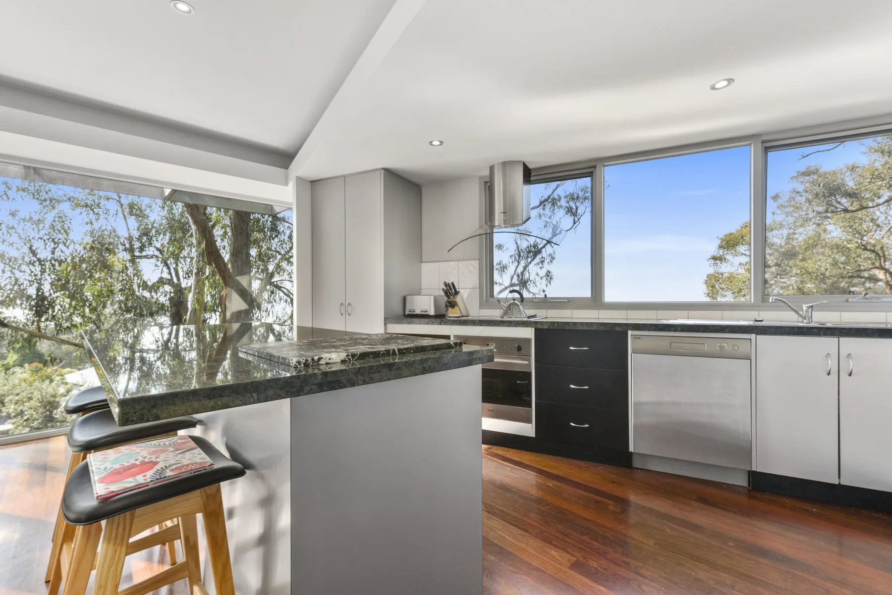 A bright kitchen with a central island and wide windows overlooking trees.