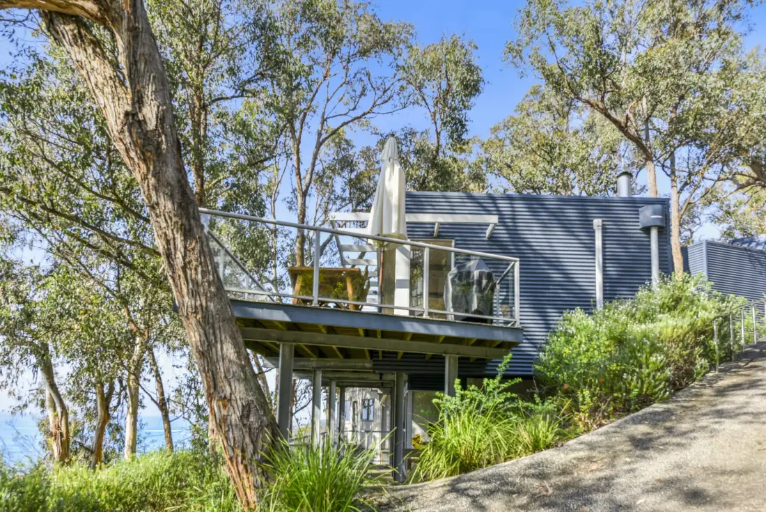 A raised building with a deck sits among trees on a sloping hillside.
