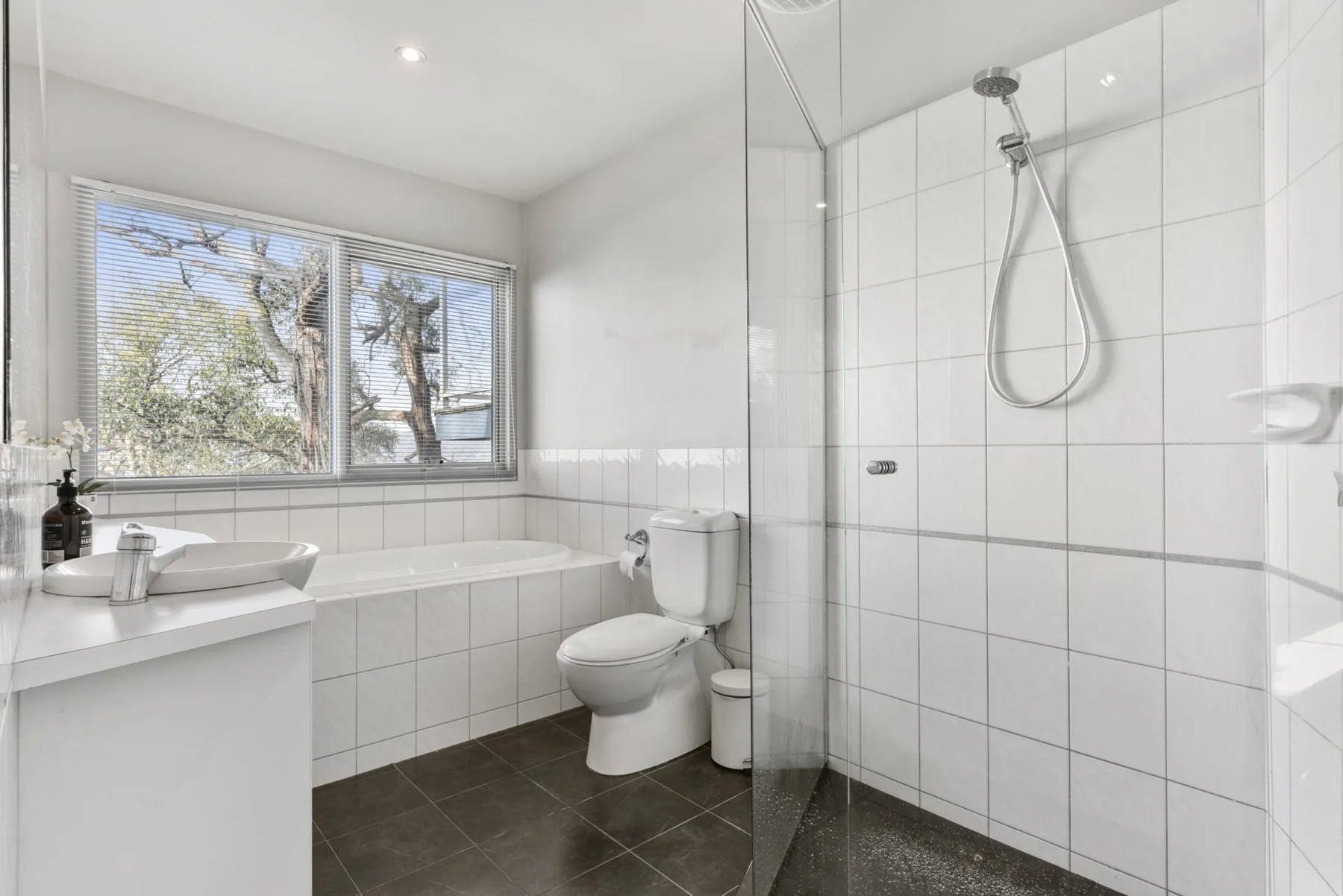 A bright tiled bathroom with a bathtub, toilet, and glass-enclosed shower.