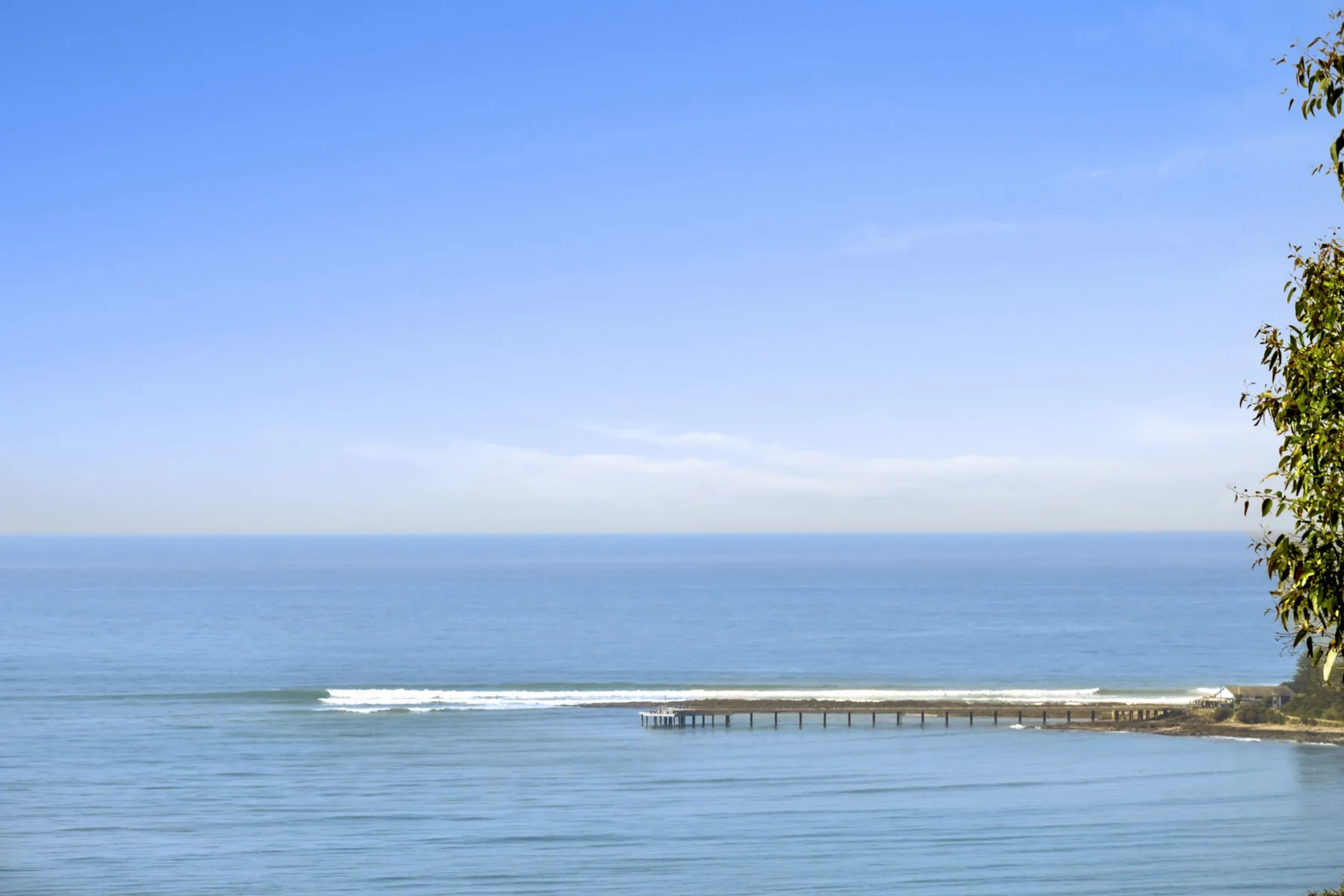 A calm seascape with a long pier extending over the water.