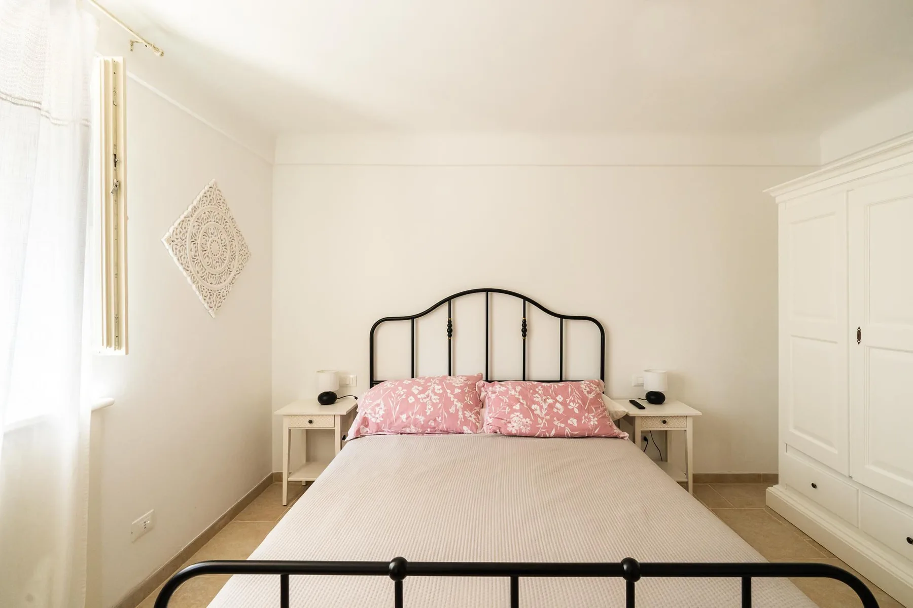 A bright bedroom with a bed, bedside tables, and a wardrobe.