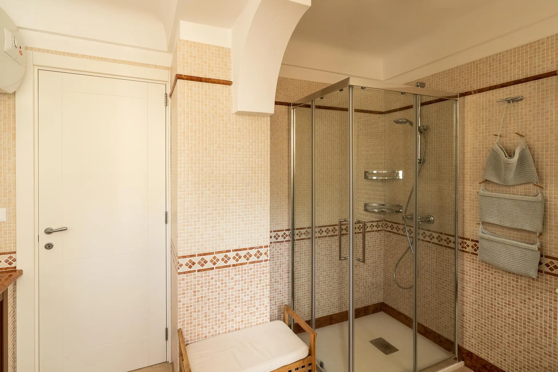 A tiled bathroom with a glass shower and a white door.