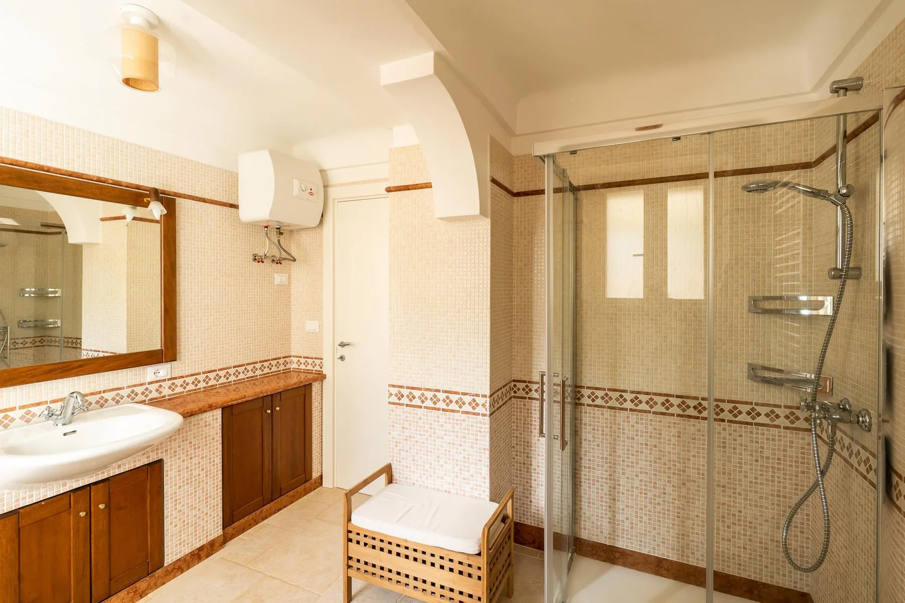A tiled bathroom with a sink, wooden vanity, and glass shower enclosure.