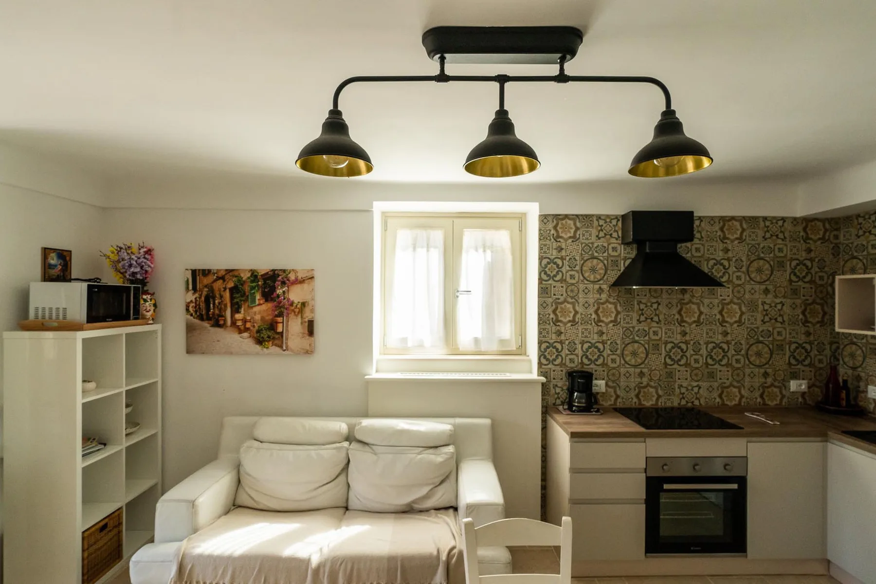 A compact living area opens into a kitchen, with a sofa beneath a bright window.
