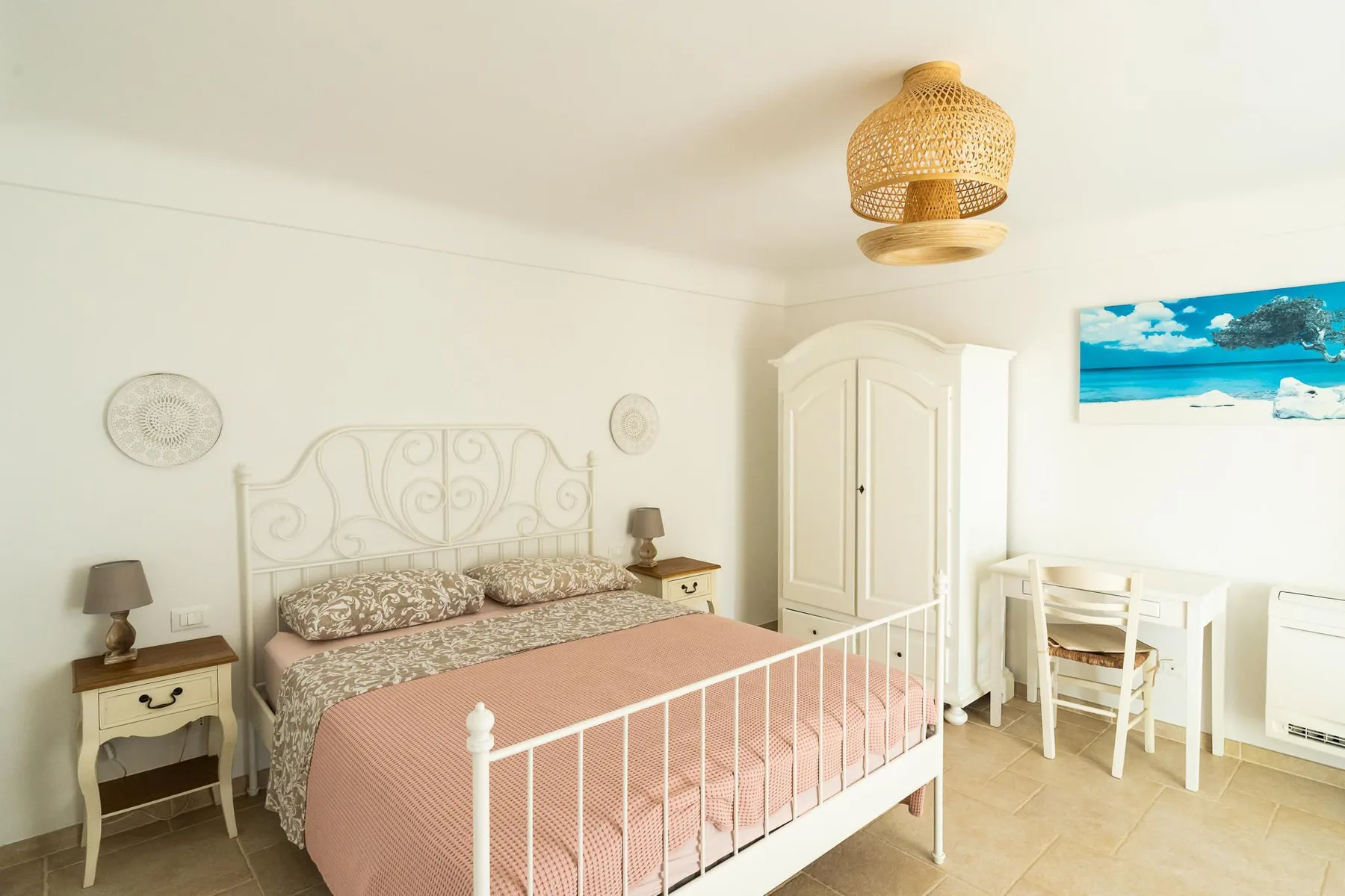 A bright bedroom with a pink bedspread and white metal bed frame.