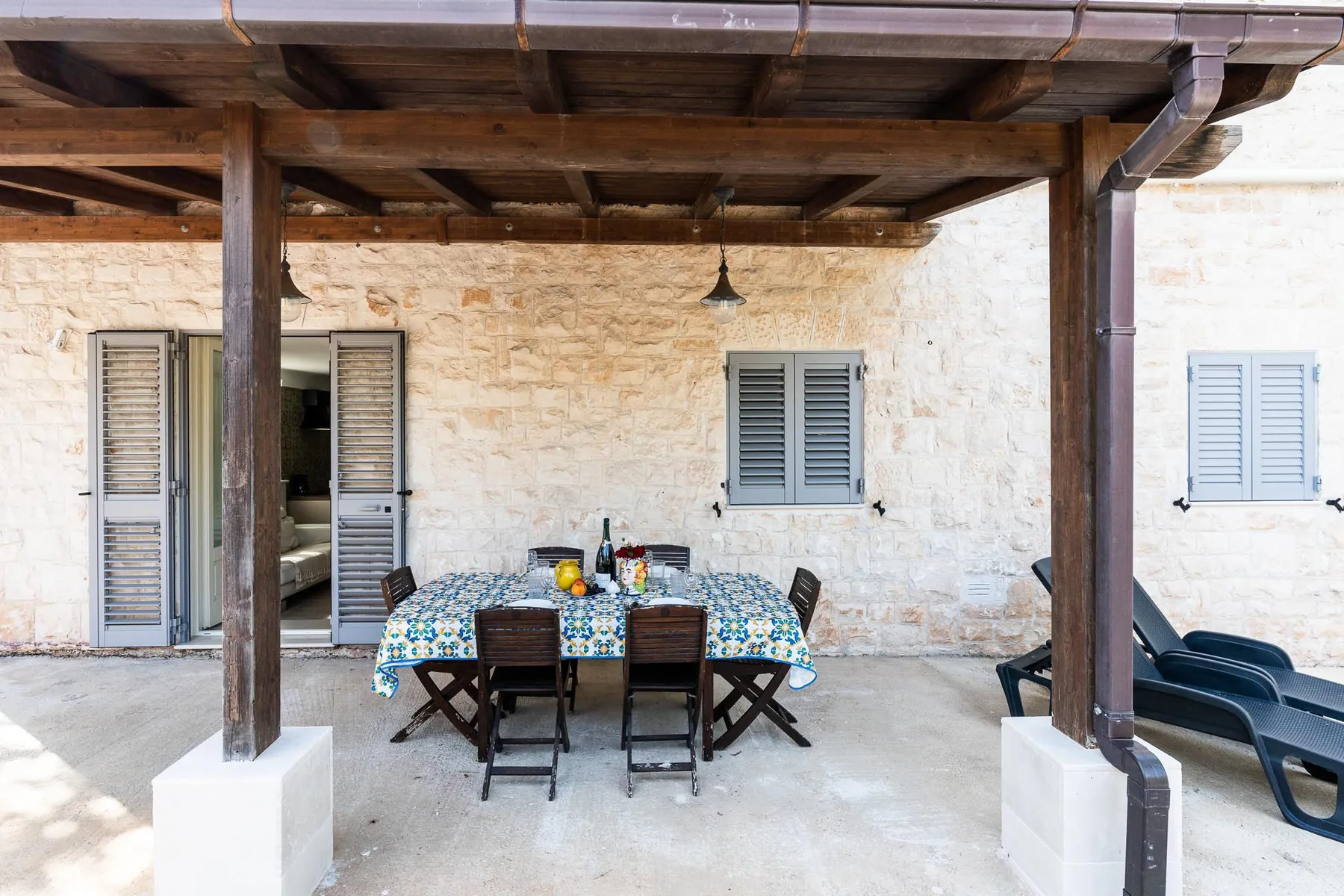 A covered outdoor dining area with a table and seating beside a stone wall.