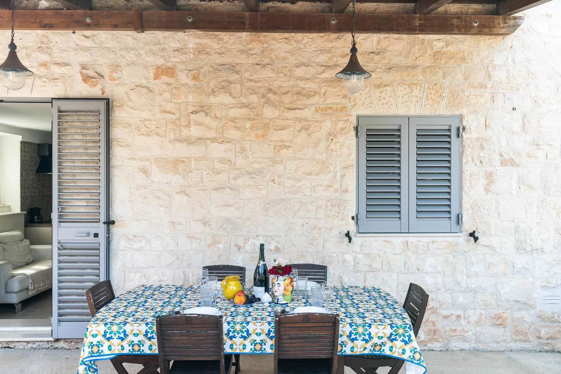 A stone-walled outdoor dining area with a table covered in a colorful patterned cloth.
